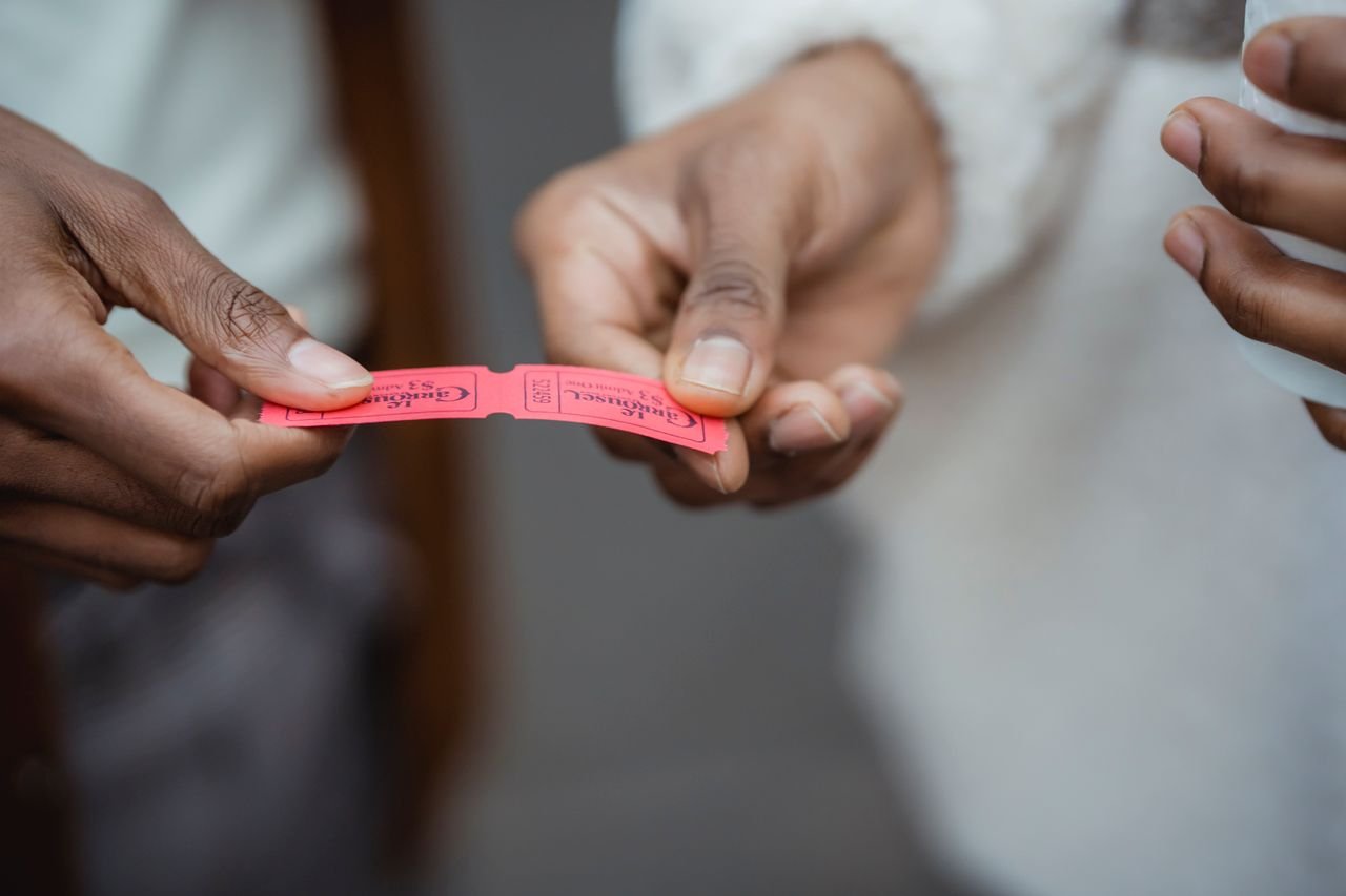 Crop unrecognizable African American friends holding small paper tickets in hands on street in daytime