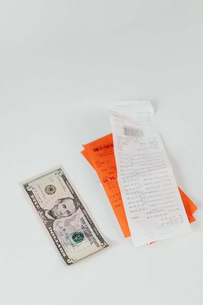 about-02 A crisp US dollar bill next to colorful shopping receipts on a clean white surface.